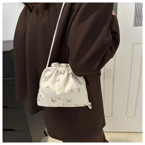 Detail of cream crossbody bag featuring floral embroidery and woven drawstring straps