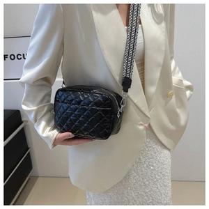 Detail of black quilted crossbody bag featuring wide pattern strap on a white blazer