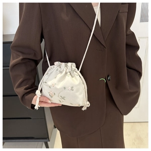 Detail of floral embroidery on beige fabric crossbody bag with white woven drawstring