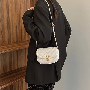 Quilted cream crossbody bag with gold horseshoe clasp and chain strap on a model