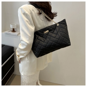 Detailaufnahme der schwarzen Stepptasche mit goldener Kette am Model im modernen Studio