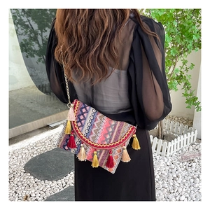 Detailed close-up of ethnic style fabric bag with colorful tassels and gold chain strap