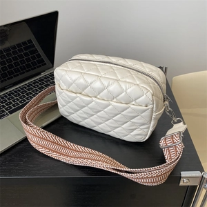 White quilted crossbody bag with stylish wide woven strap on minimalist office desk