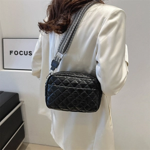 Black quilted crossbody bag with geometric wide strap shown on a white blazer model
