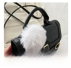 Detail einer schwarzen Handtasche in Krokostruktur mit weißem Kunstfell-Pompon-Anhänger