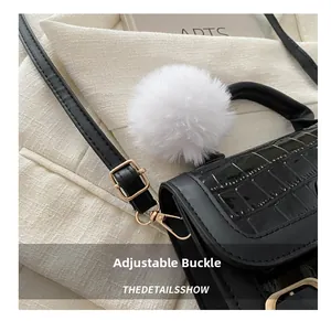 Details einer schwarzen Handtasche in Krokodilleder-Optik mit Plüschball und Goldschnalle