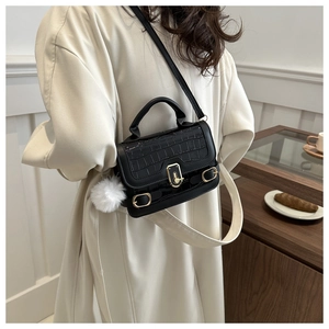 Close-up of black crocodile embossed small bag with golden lock and plush ball