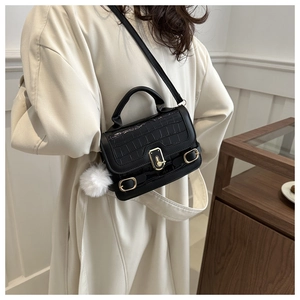 Detail of black faux crocodile leather mini bag with metal clasp and plush ball charm