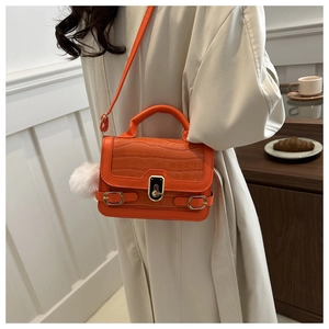 Detail of bright orange crossbody bag with crocodile texture, gold lock and white pompom