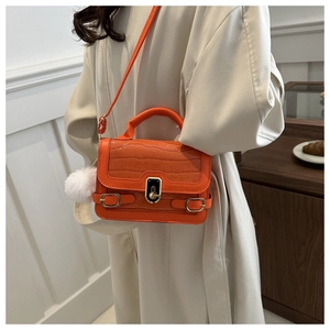 Detail der leuchtend orangefarbenen Handtasche mit Krokostruktur und Plüsch-Anhänger