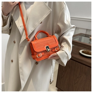 Detail der orangefarbenen Crossbody-Tasche mit Krokomuster und goldenem Drehverschluss