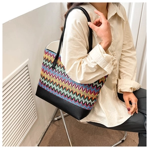 Detail of colorful woven straw tote bag featuring wavy patterns and black leather bottom