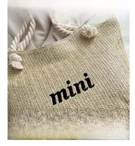 Detail of woven straw tote bag featuring mini embroidery and thick rope handle design