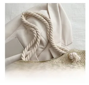 Detail of woven straw tote bag featuring thick cotton rope handles and metal eyelet accents