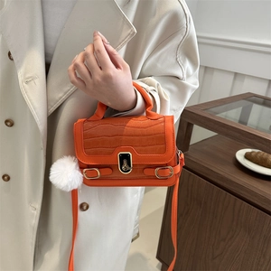 Orange croc-embossed mini square bag with gold lock and plush charm on trench coat