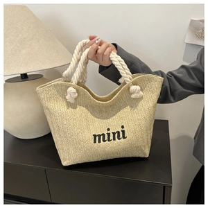 Close-up of a beige straw woven handbag featuring black mini embroidery and rope handles