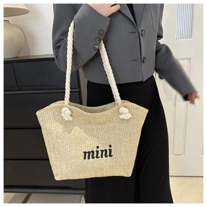 Detail of hand-woven straw bag featuring white rope handle and mini embroidery text