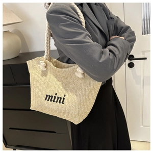 Detail of woven straw tote bag featuring mini embroidery and white cotton rope handles
