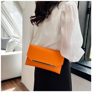Detail der orangefarbenen Umschlagtasche mit Plissee, Goldleiste und Kettenriemen