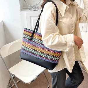 Bohemian colorful woven straw tote bag with black leather handles carried by a model