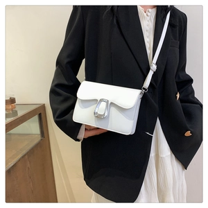 Close-up of stylish white crossbody bag with large silver metal buckle and long strap