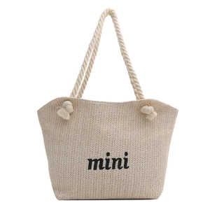 Large beige woven straw tote bag with rope handles and mini text for summer beach trips