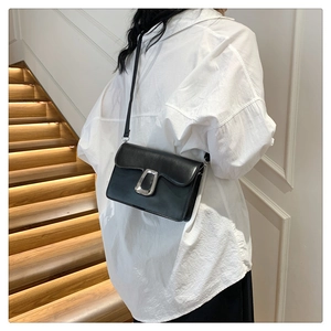 Close-up of minimalist black leather crossbody bag with silver U-shaped metal buckle detail