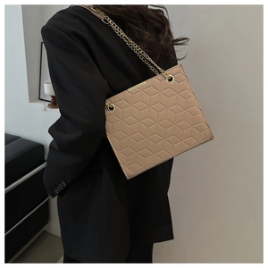 Detail of beige quilted shoulder bag with gold chain strap worn on a black blazer