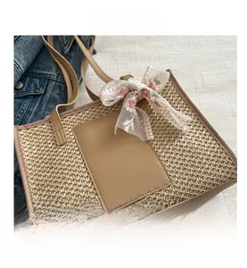 Detail of straw woven tote bag featuring beige lace embroidery and leather handles