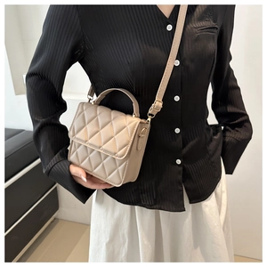 Détail du sac carré matelassé beige avec ferrures dorées et poignée sur le dessus