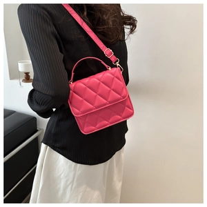 Détail du sac bandoulière matelassé rose rouge avec finitions dorées porté à l'épaule