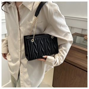 Close-up of black quilted shoulder bag with V-shaped stitching and gold chain strap
