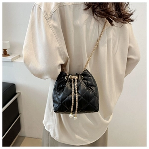 Detail view of quilted black bucket bag with gold chain and white pearl drawstring accents