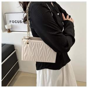 Detail of beige quilted shoulder bag featuring V-shaped texture and gold metal chain