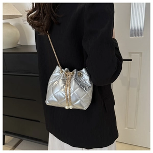 Silver quilted bucket bag featuring pearl drawstrings and golden chain on a model