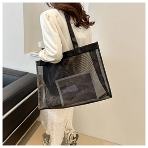 Detail shot of a large black mesh tote bag carried by a model in a minimalist modern room
