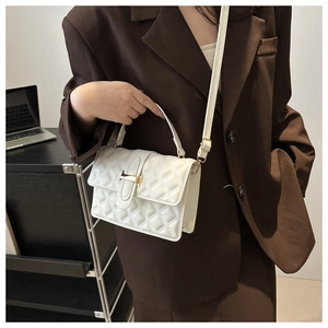 Close-up of white quilted crossbody bag with elegant gold H-shaped metal buckle detail