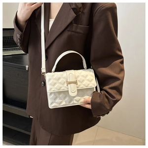 Detail of white quilted crossbody bag featuring a gold H-buckle and elegant leather strap
