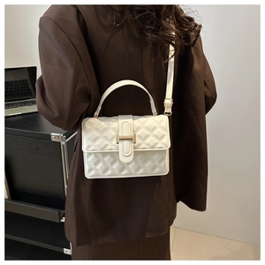 Close-up of white quilted crossbody bag with gold buckle on a brown blazer model