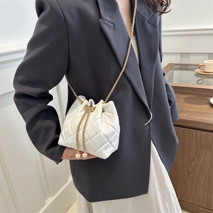 Chic white quilted bucket bag with gold chain strap and pearl accents on a female model