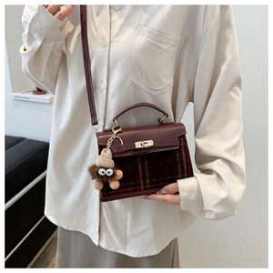 Detail of burgundy leather and plaid fabric crossbody bag with a cute plush monster charm