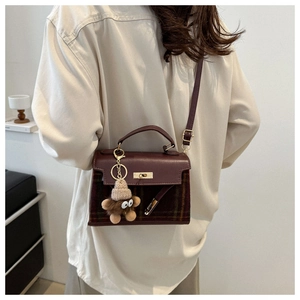 Detail of vintage plaid handbag with leather flap and cute plush charm on shoulder strap