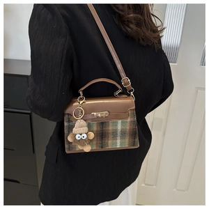 Detailed view of checkered wool and brown leather handbag with a cute plush monster charm
