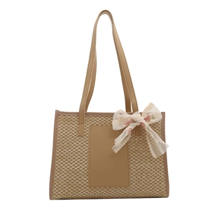 Straw woven tote bag with faux leather straps and a floral lace bow accent for beach travel