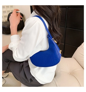 Detail of royal blue crescent bag with crocodile pattern and gold hardware on shoulder