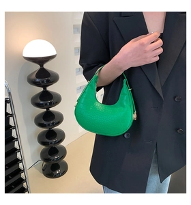 Detail of bright green crescent bag with crocodile texture and gold hardware on black suit