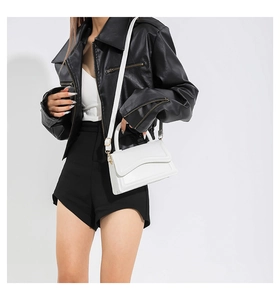 Detailed side view of a white leather square crossbody bag with gold hardware on a model