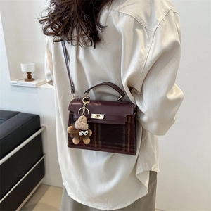Elegant burgundy plaid handbag with top handle and bear charm in a modern minimalist interior