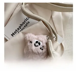 Close-up of pink plush square charm with embroidered face on off-white leather bag