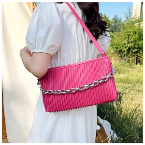 Detail of magenta pleated shoulder bag with decorative silver chain on a model